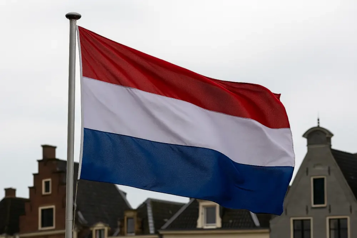Nederlandse vlag wappert aan een zilveren vlaggenmast voor historische gebouwen in Leeuwarden onder een bewolkte lucht
